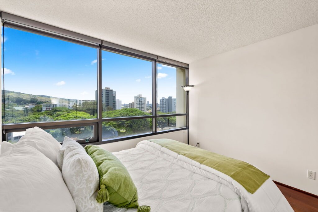 Bright secondary bedroom with large windows overlooking treetops and cityscape.