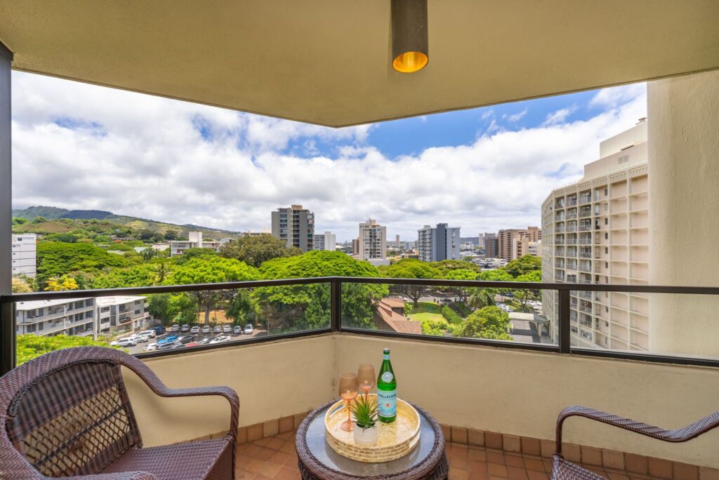 Covered lanai overlooking lush treetops, mountains, and city views.